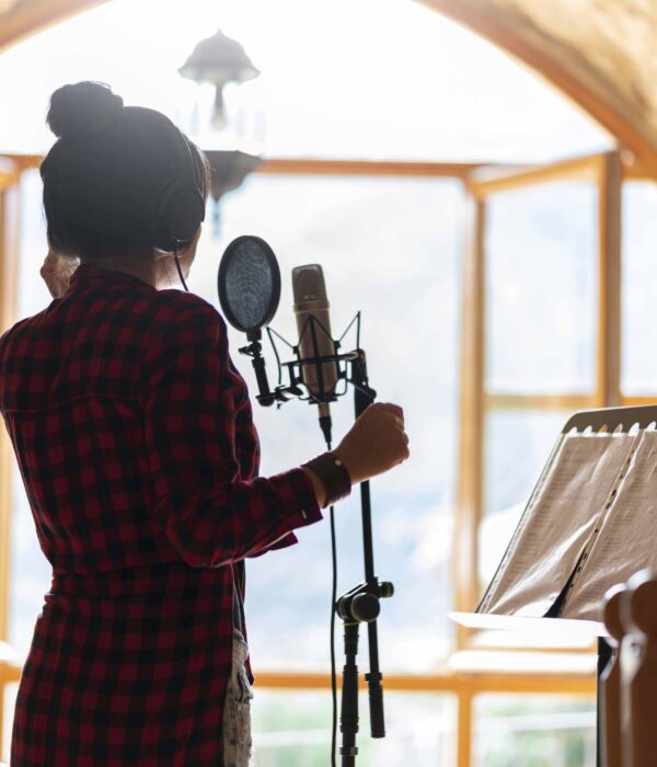 Young brunette woman, professional singer recording a song in a studio with a microphone and headphones